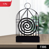 A black iron birdcage-style holder with a burning mosquito coil is on a wooden table, with a red