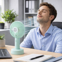 Portable handheld fan cooling a user at an office desk, perfect as a personal cooling device.
