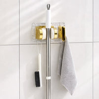 Space saving broom and mop hanger wall mounted with self adhesive base