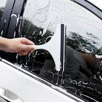 A hand uses a white car mirror wiper to clean a car window, leaving streaks in the white suds.