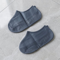 Two navy blue silicone shoe covers are laid flat on a light grey tiled surface, showcasing their textured soles.