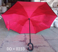 An open, bright red reverse umbrella with a C-shaped handle is displayed on a concrete floor in a warehouse setting.